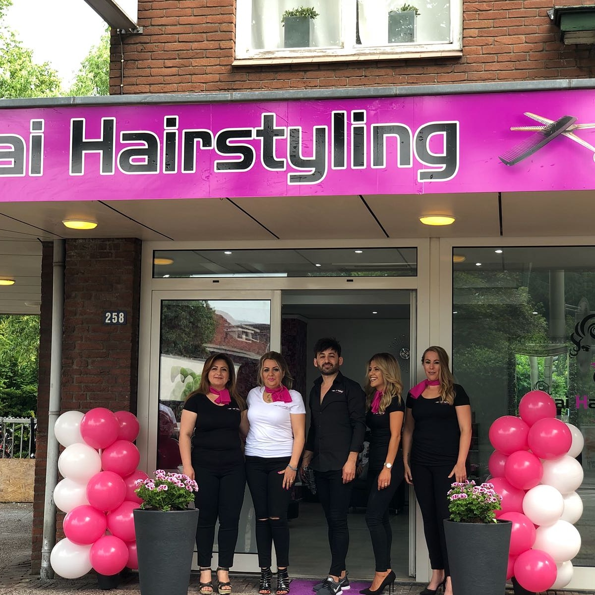 Het team voor het roze gevelbord van Luai Hairstyling aan de Groenestraat